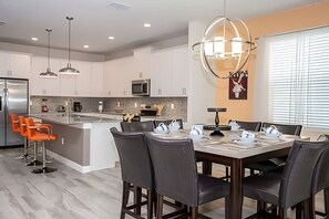 A modern kitchen with white cabinets, a central island, and a dining area with a table and chairs. - 6BR Townhome w/ Pool 10 Min to Disney (Kissimmee)
