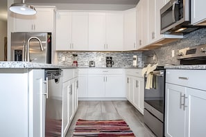 Une cuisine moderne avec des armoires blanches, un pare-feu en pierre et des appareils électroménagers en acier inoxydable.