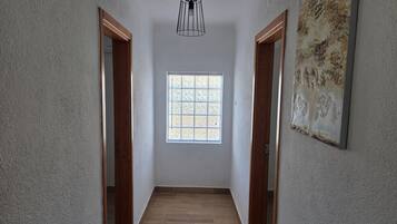 A hallway with wooden doors, a window with blinds, and a hanging light fixture.