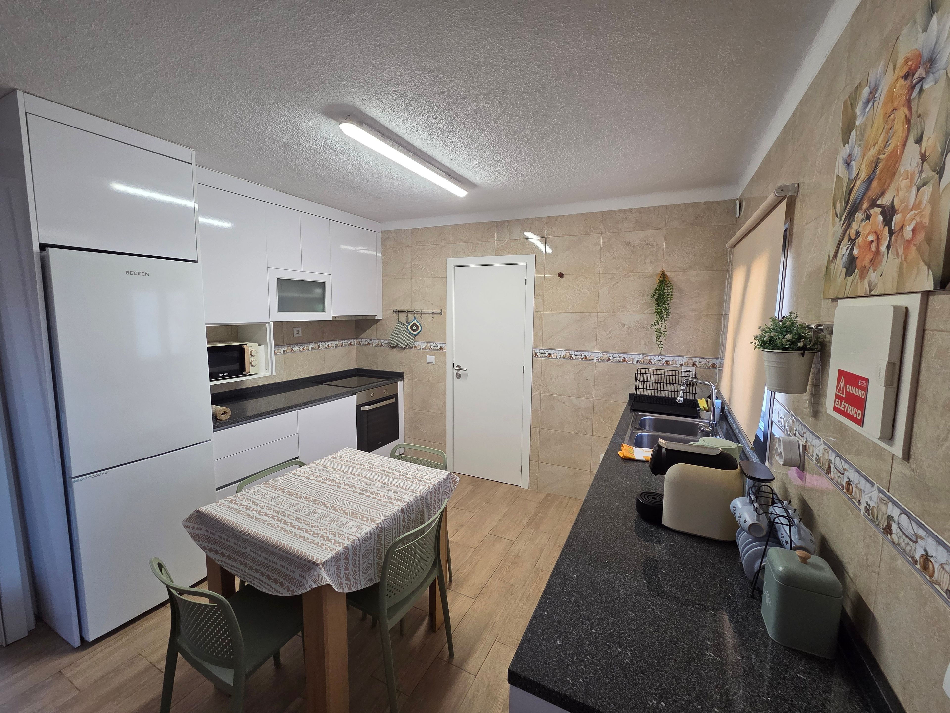 Cocina compacta con armarios blancos, horno empotrado, lavamanos y comedor con mesa y sillas.