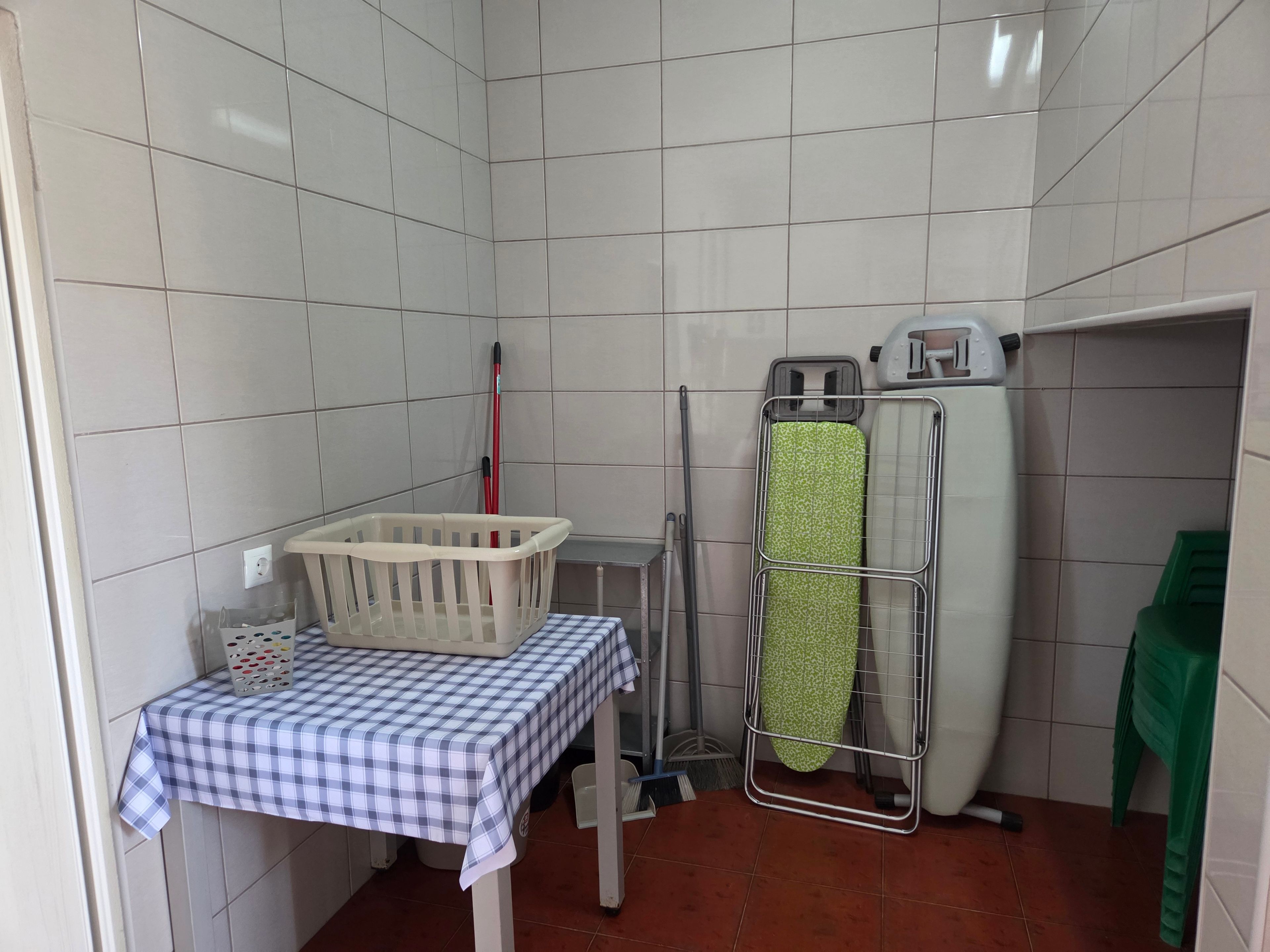 Et lille vaskerum med et bord, en tørrestativ, en kurv og rengøringsudstyr.