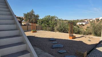 A residential outdoor area with a concrete staircase, gravel ground, stepping stones, wooden planters, and a fence.
