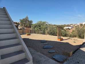 A residential outdoor area with a concrete staircase, gravel ground, stepping stones, wooden planters, and a fence. - Casa Olival de Mares - Alentejo (Casas Novas de Mares)