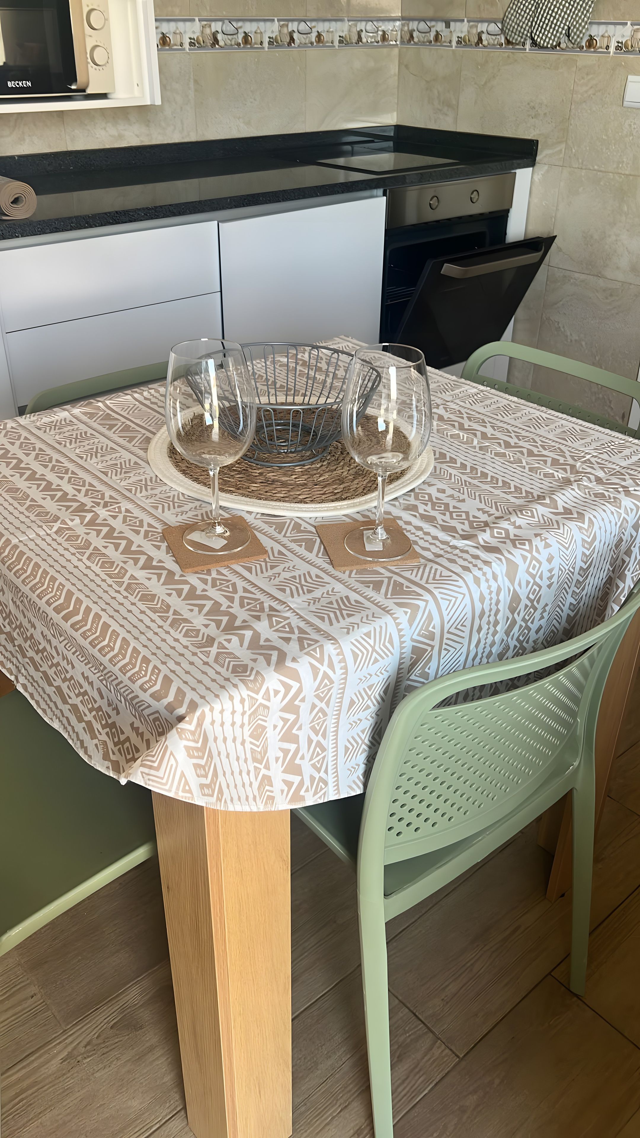 A dining table with a patterned tablecloth, two wine glasses, and a woven placemat.