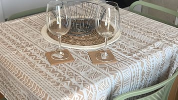 A dining table with a patterned tablecloth, two wine glasses, and a woven placemat.