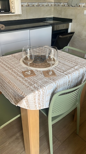 A dining table with a patterned tablecloth, two wine glasses, and a woven placemat.