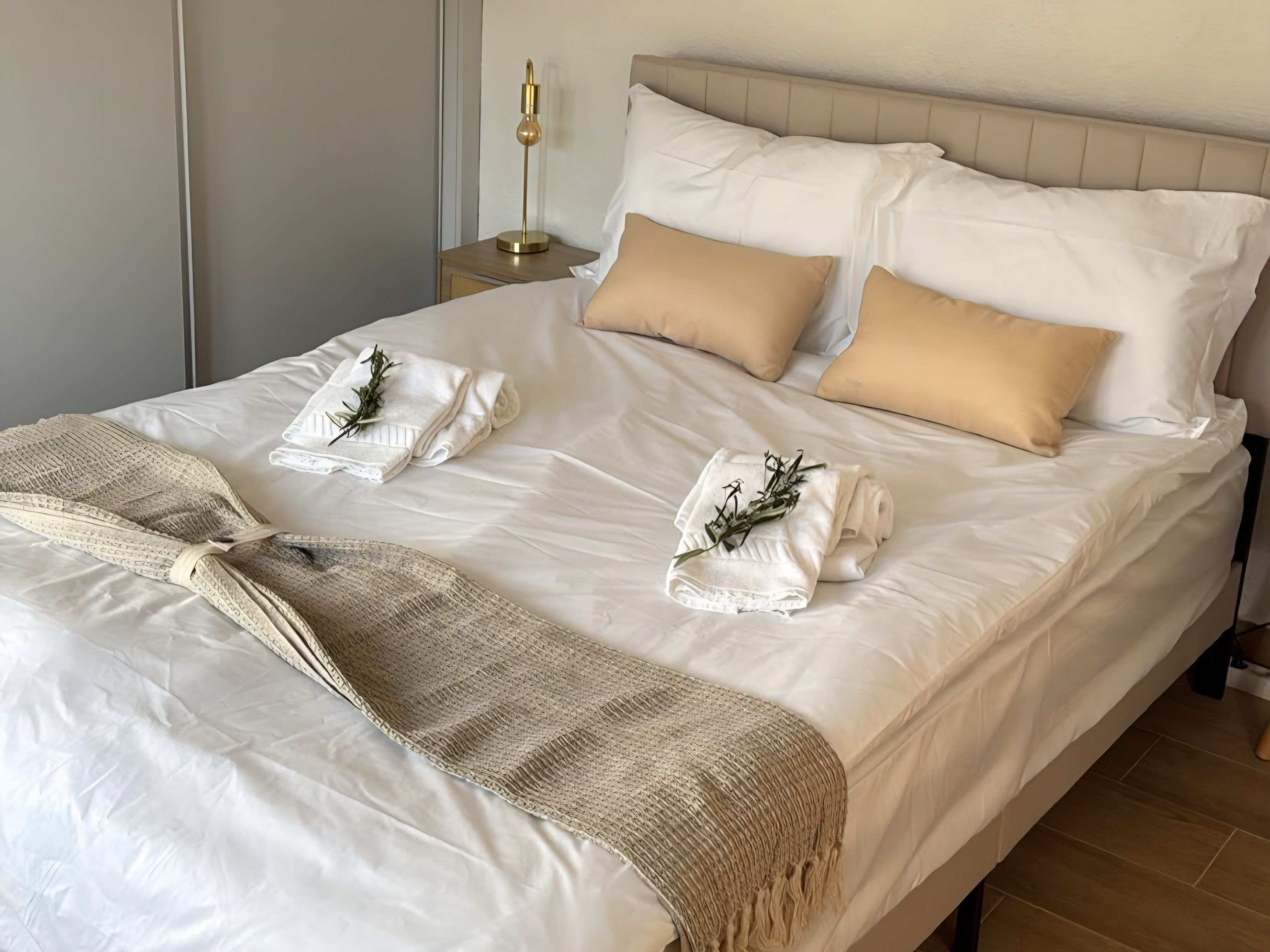 En pænt redt seng med hvide sengetøj, to beige puder og et beige tæppe.