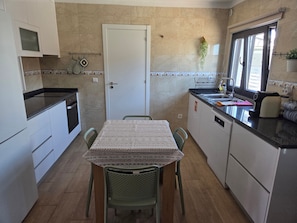 A compact kitchen with a dining table, chairs, a stove, and a sink. - Casa Olival de Mares - Alentejo (Casas Novas de Mares)