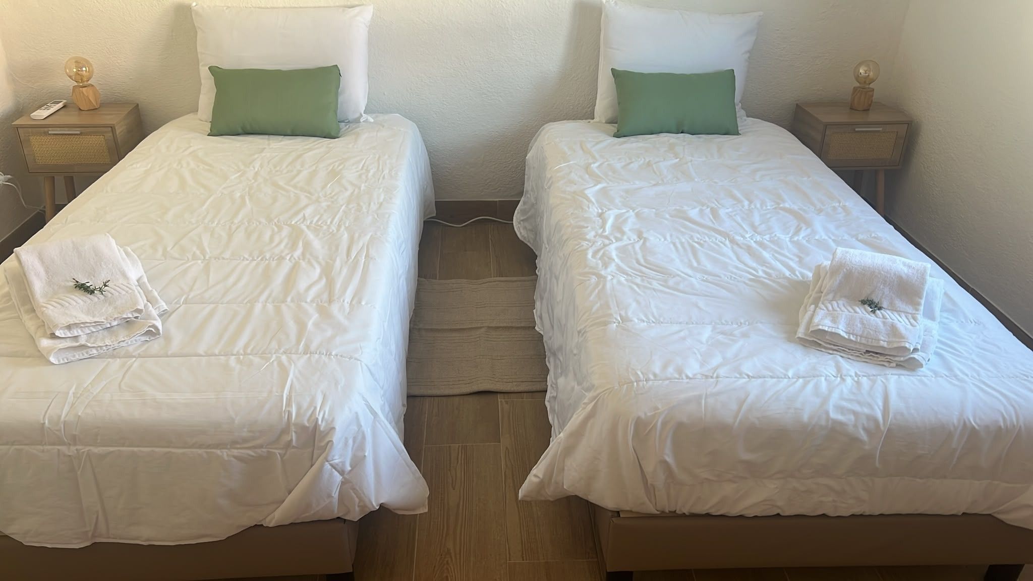 Two single beds with white bedding, green pillows, and folded white towels on each bed.