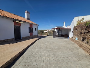 A paved street with buildings on either side, a clear sky, and a stone wall on the right. - Casa Olival de Mares - Alentejo (Casas Novas de Mares)