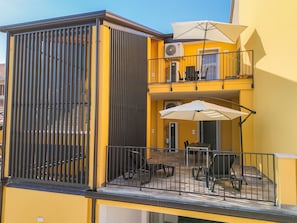 Un bâtiment jaune doté d’un balcon, d’une terrasse et d’un espace extérieur couvert avec des parasols.