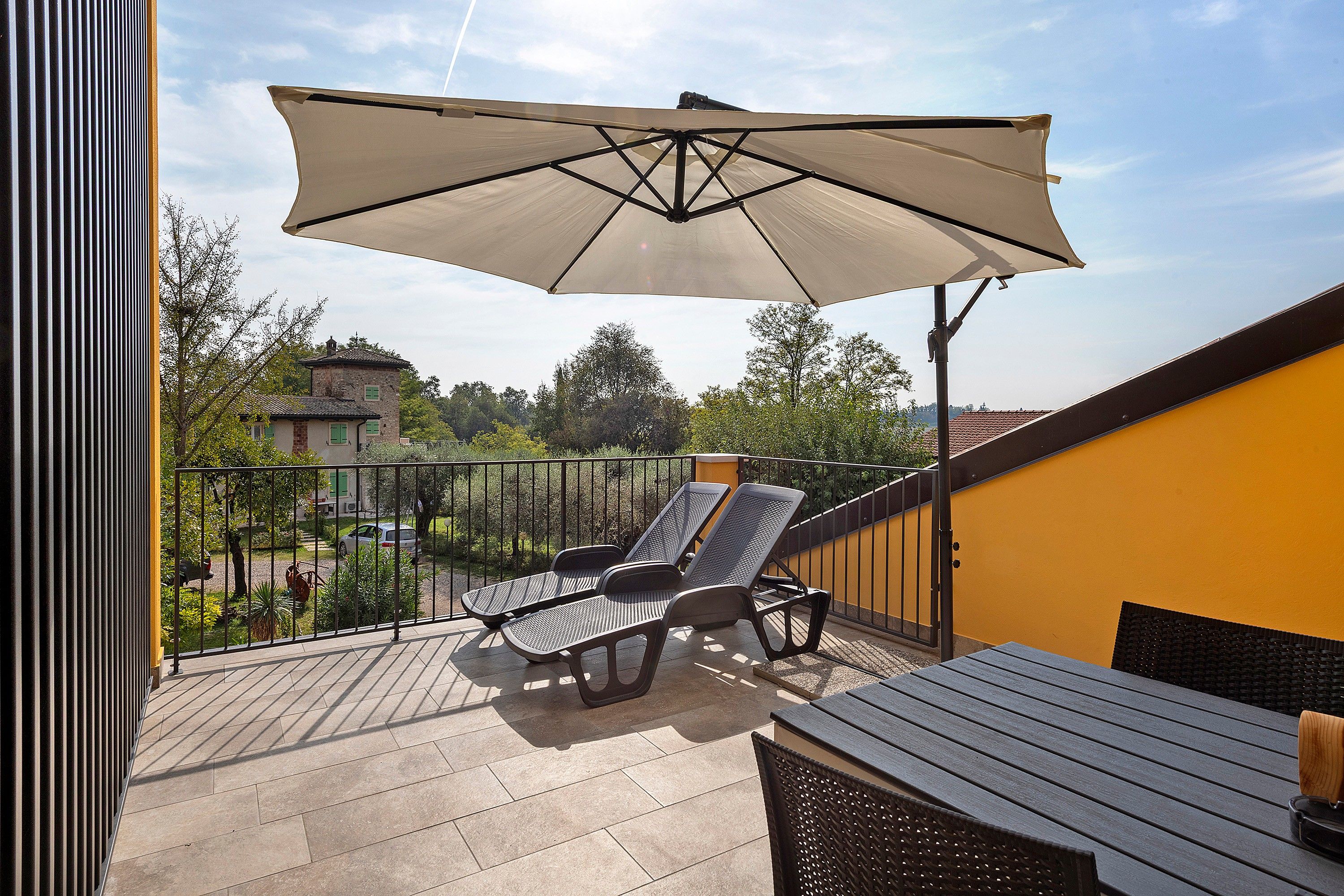 A balcony with a table and two chairs, an umbrella, and a view of the surrounding area.