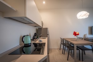 Une cuisine moderne équipée d’une cuisinière intégrée, d’une bouilloire et d’une machine à café. On y trouve une table à manger avec des chaises et un vase rempli de fleurs.