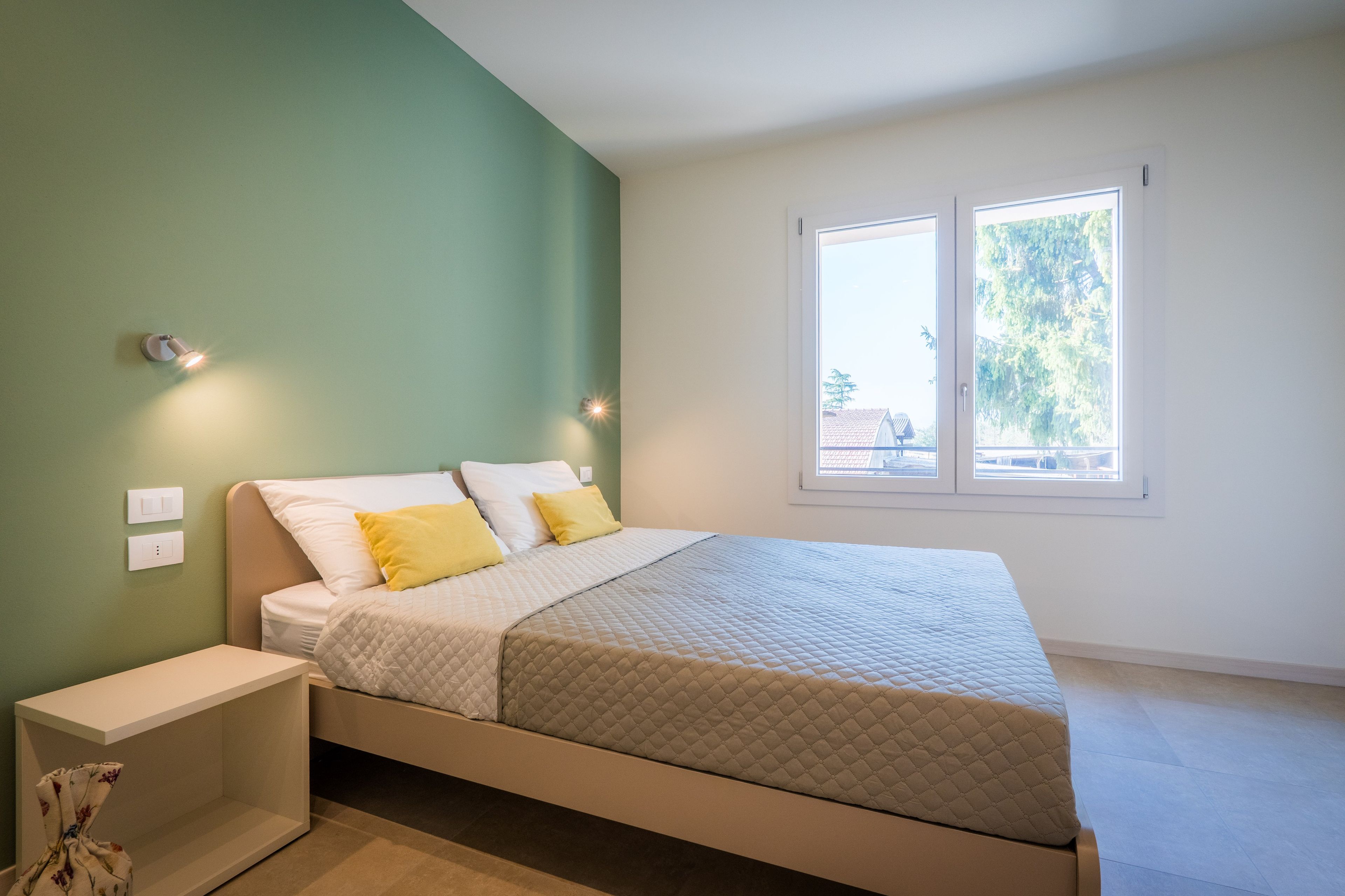 Une chambre à coucher avec un lit, des tables de chevet, une fenêtre et une vue sur l’extérieur.