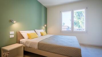 Un dormitorio con cama, mesitas de noche, una ventana y vistas al exterior.