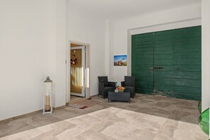 A hallway with a green door, a white wall, a small table with a vase, and a chair.