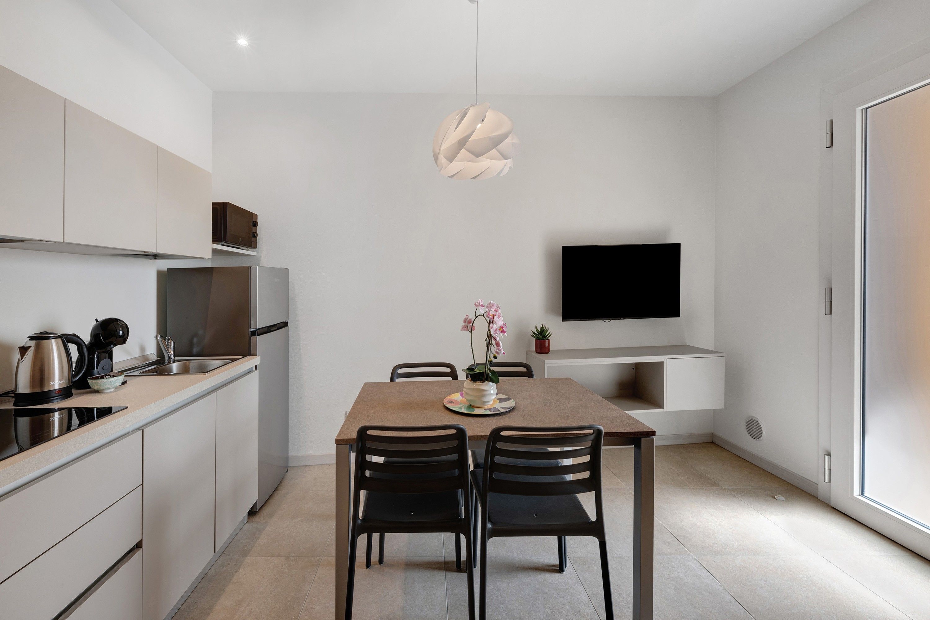 Et moderne køkken med spiseplads, et fladskærms-tv på væggen og minimalistisk indretning.