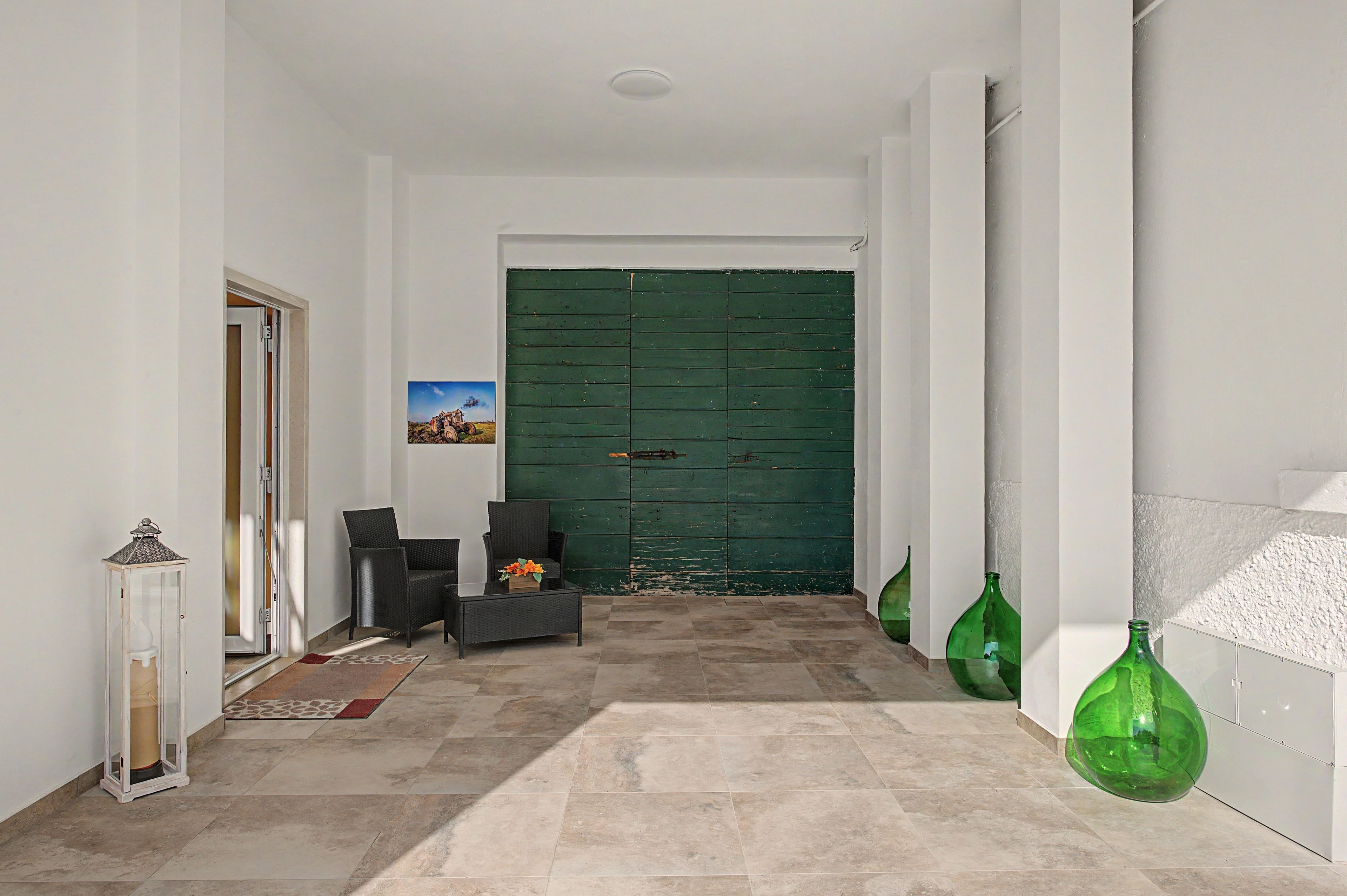A hallway with a green door, a small table with a flower arrangement, and two green glass bottles.