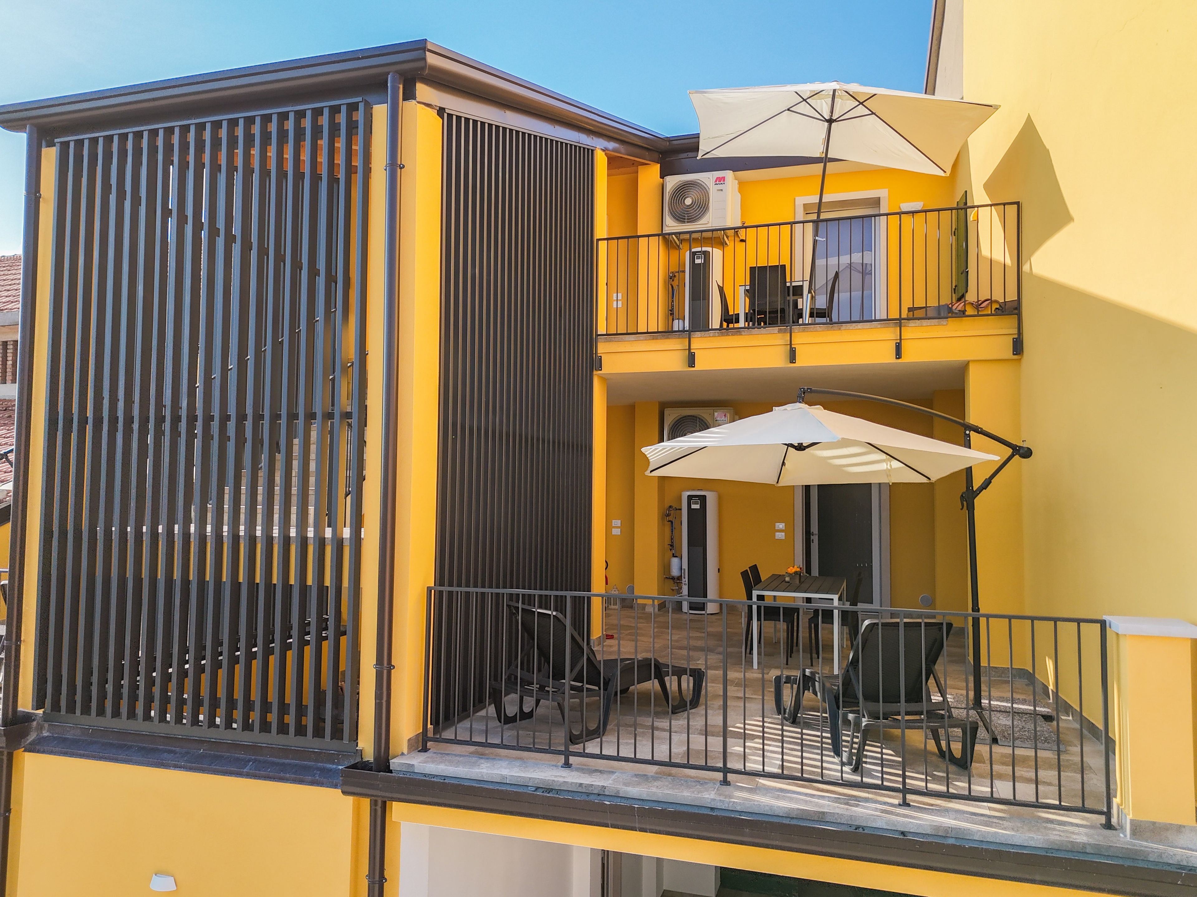 A yellow building with a balcony, outdoor seating, and a covered area with umbrellas.