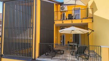 A yellow building with a balcony, outdoor seating, and a covered area with umbrellas.