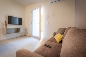 Un salon équipé d’un téléviseur à écran plat, d’un canapé avec un coussin jaune et d’une porte-fenêtre coulissante.