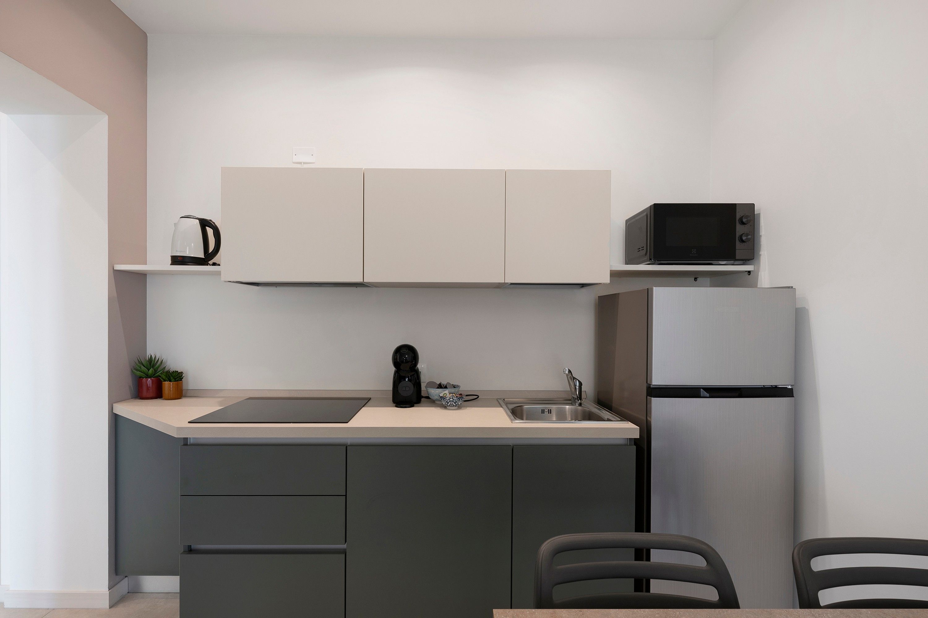A compact kitchen with a built-in microwave, a coffee machine, and a refrigerator.