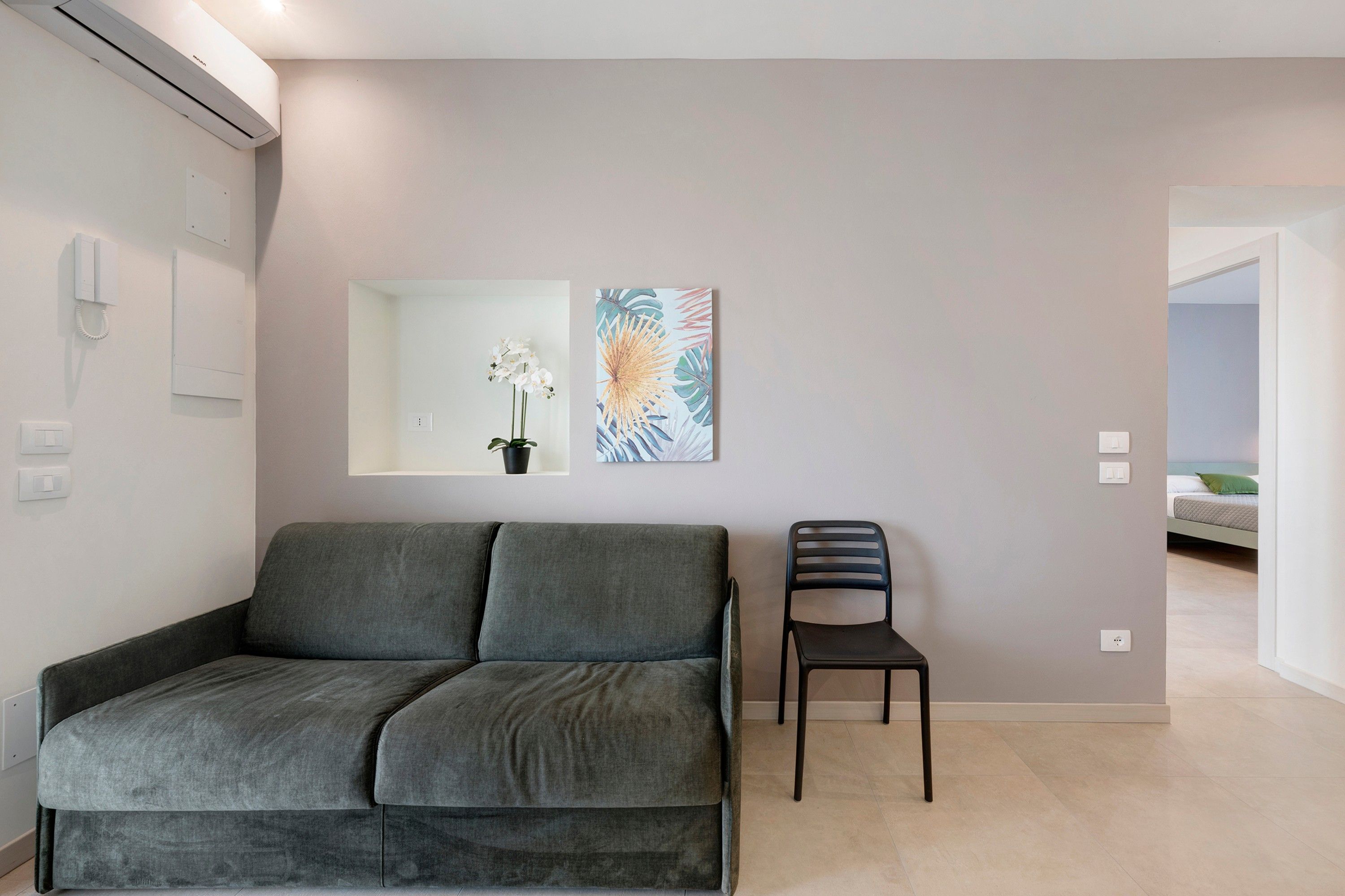 Una sala de estar moderna con un sofá gris, una silla negra y una obra de arte colgada en la pared.