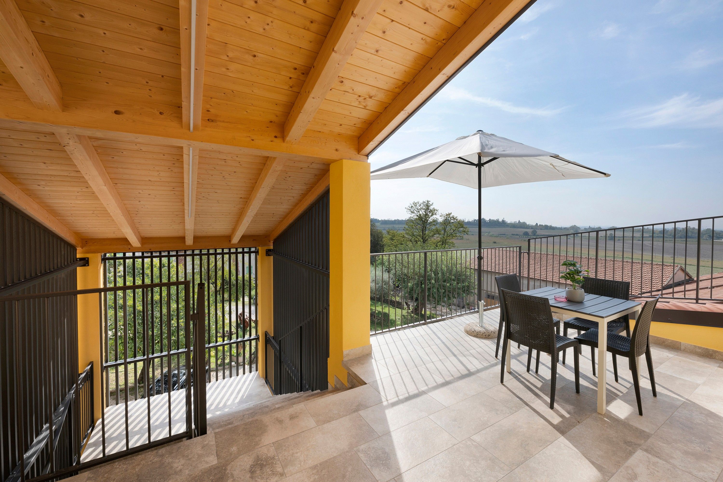 A balcony with a table and chairs, a white umbrella, and a view of the countryside.