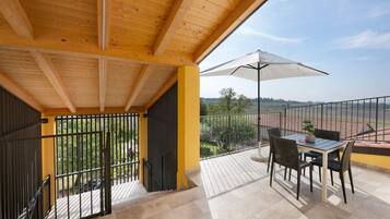 A balcony with a table and chairs, a white umbrella, and a view of the countryside.