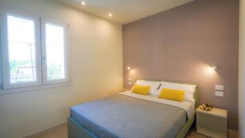 Un dormitorio con cama, dos lámparas de noche, una ventana y una mesita de noche con un arreglo floral.