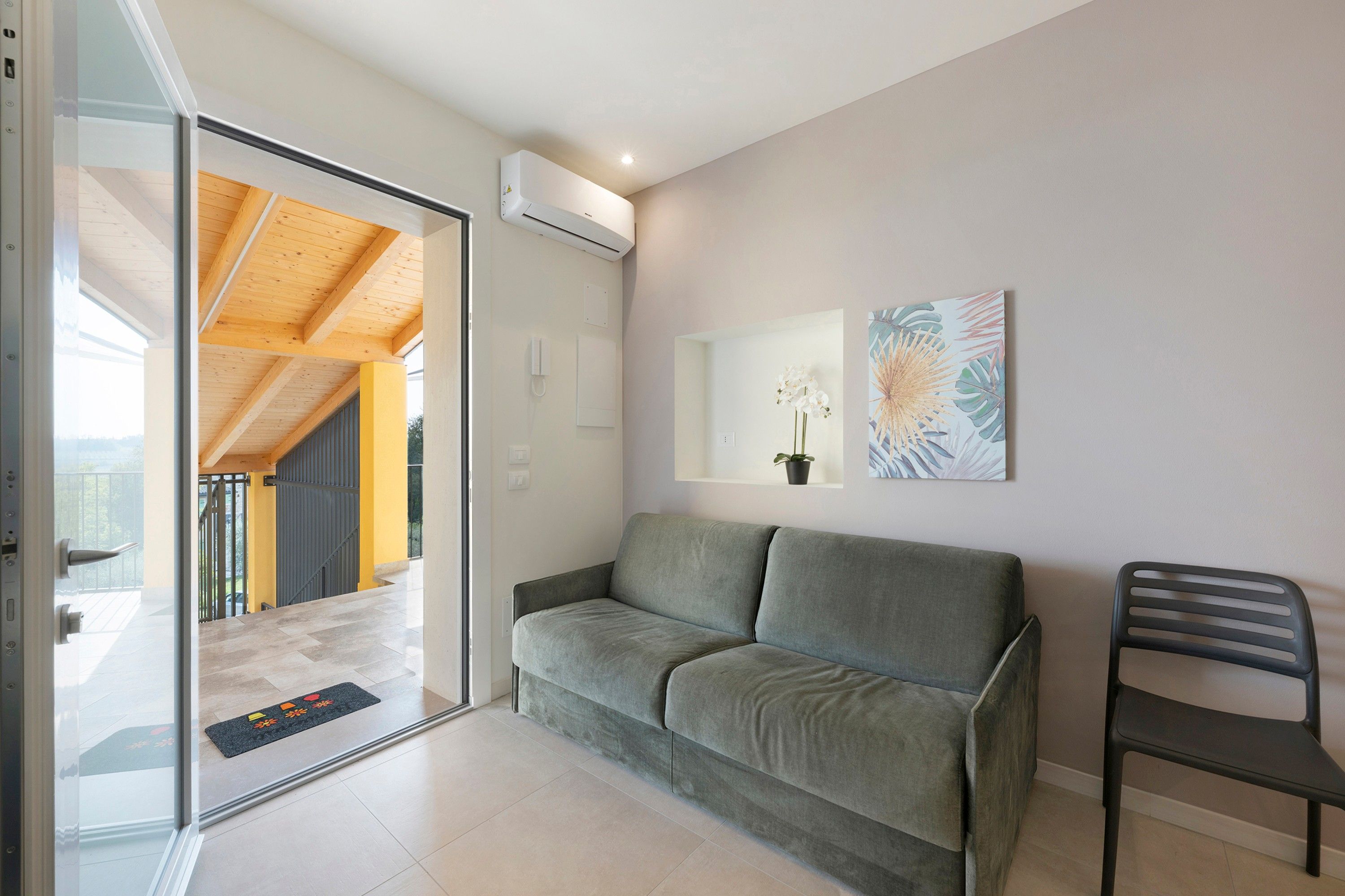 A modern living room with a grey sofa, a black chair, and a wall-mounted air conditioner.