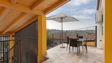 Un balcón con una mesa y sillas, una sombrilla blanca y vistas al campo.