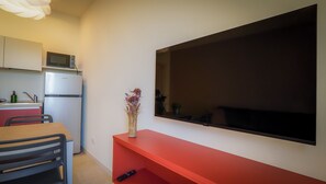 Une cuisine compacte équipée d’un réfrigérateur, d’un four à micro-ondes et d’un petit évier. Un téléviseur à écran plat est fixé au mur, au-dessus d’une étagère rouge.