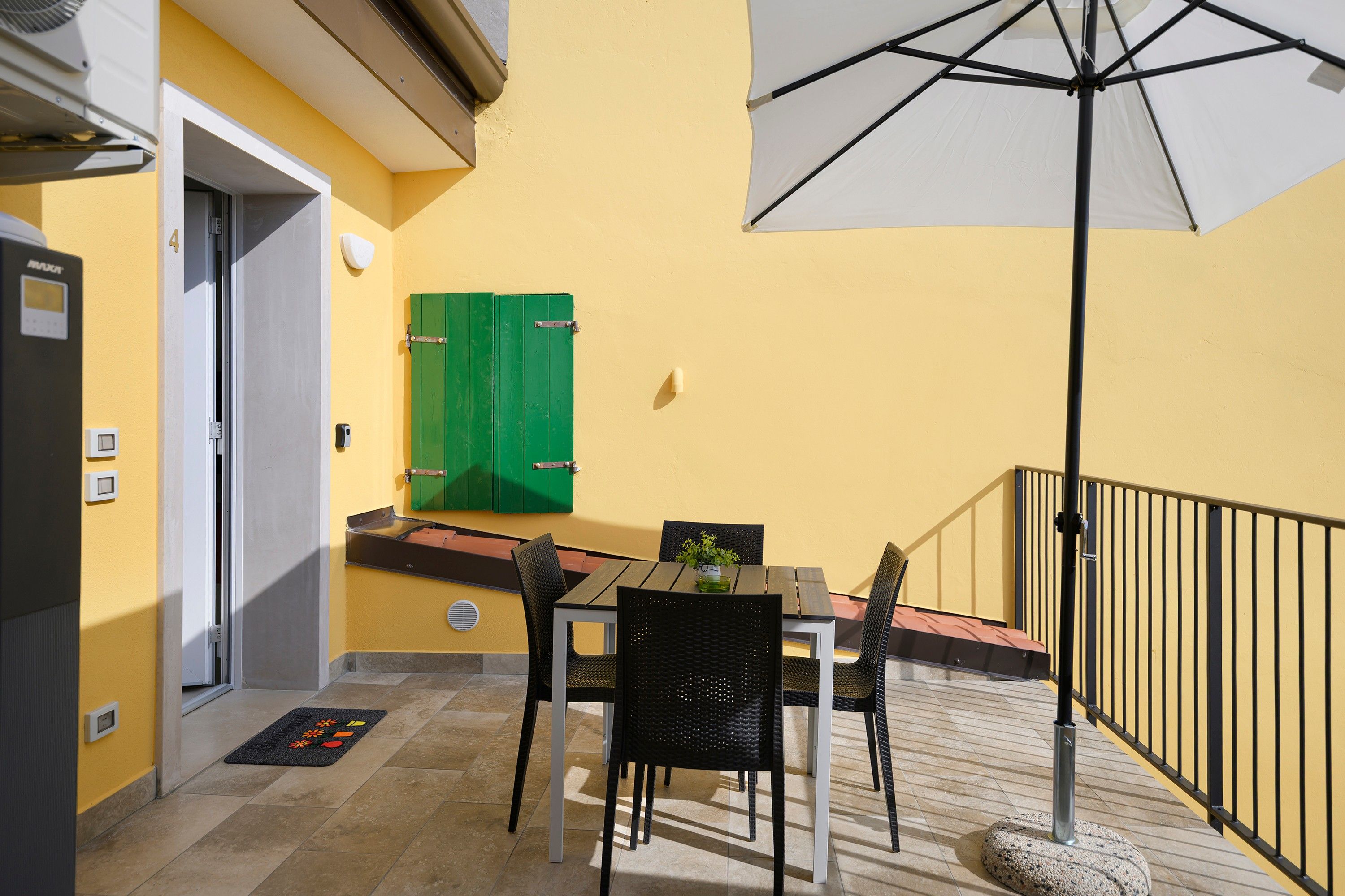 A patio with a table and chairs, a green shutter door, and a white umbrella.
