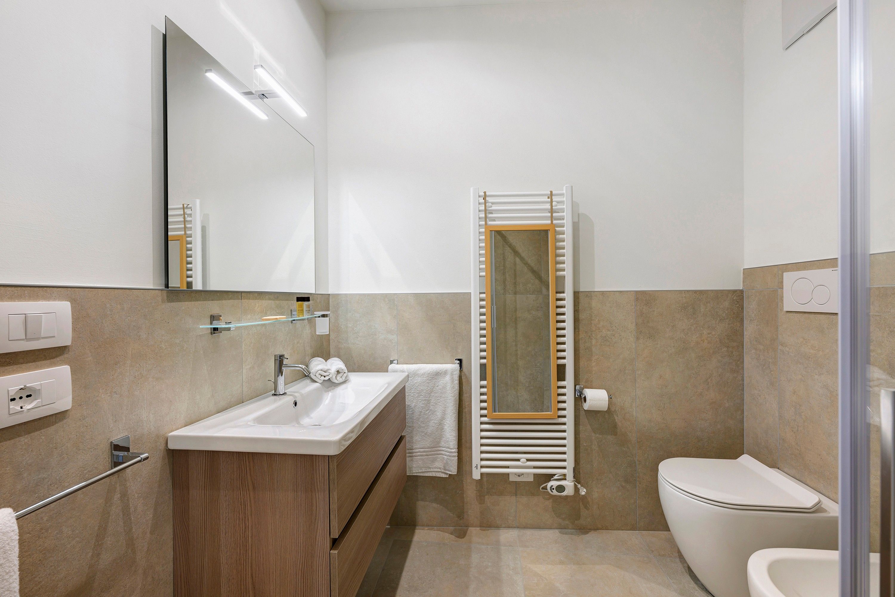Un bagno moderno con lavandino, specchio, porta asciugamani e water.