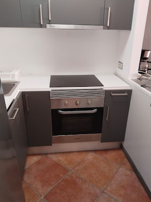 Eine kleine Küche mit Backofen, Kochfeld und grauen Schränken.