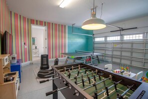 A room with a foosball table, a ping pong table, and a colorful striped wall. - 6BR near Disney | Pool, spa & 2 game rooms (Kissimmee)