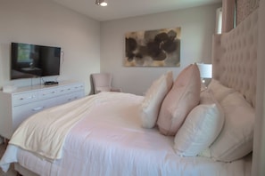 A bedroom with a large bed, a flat-screen TV, a dresser, and a painting on the wall. - 6BR near Disney | Pool, spa & 2 game rooms (Kissimmee)