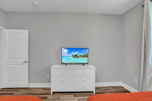 A hotel room with a white dresser, a television on top, and a door to the left. - 2BR condo near Disney | Resort with pool (Kissimmee)