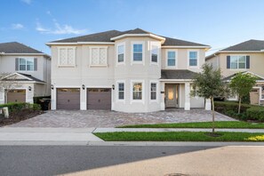A two-story residential building with a symmetrical facade, a central entrance with a door, and a garage. - 11BR near Disney | Pool, spa & home theater (Kissimmee)
