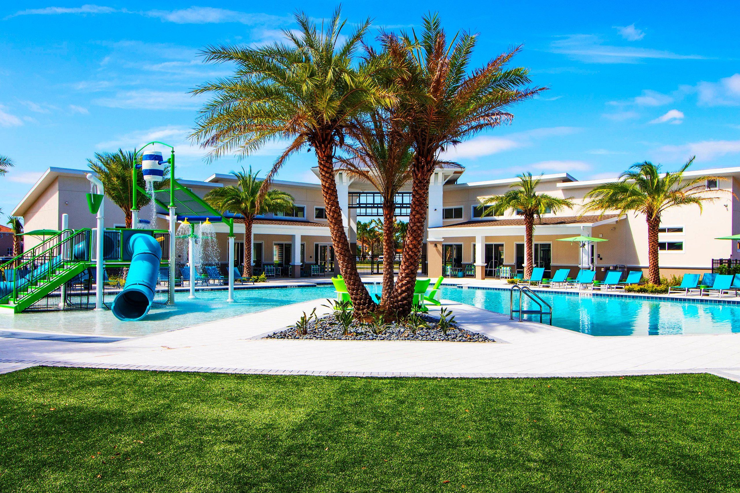 A pool area with a water slide, palm trees, and lounge chairs.