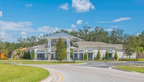 A modern building with a covered entrance, surrounded by greenery and a clear sky. - 8BR near Disney | Private pool, spa & game room (Kissimmee)