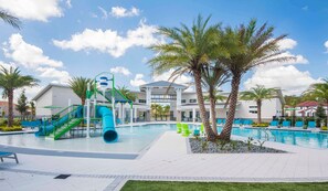 A swimming pool area with a water slide, palm trees, and a building in the background. - 8BR near Disney | Private pool, spa & game room (Kissimmee)
