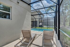 Un espacio exterior cubierto con piscina, dos sillas y vista a una casa a través de un cerramiento de vidrio.