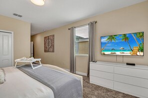 Ein Schlafzimmer mit einem Bett, einem an der Wand befestigten Fernseher, einem Schreibtisch und einem Fenster mit Jalousien.