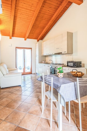 Una cocina moderna con armarios blancos, una mesa de comedor con sillas, un sofá y un ventanal con cortinas.