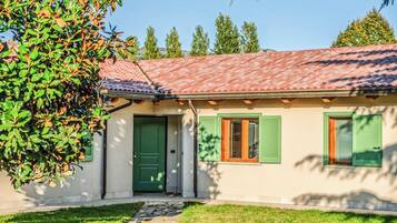 Una casa con techo de tejas, puerta verde y contraventanas en las ventanas.