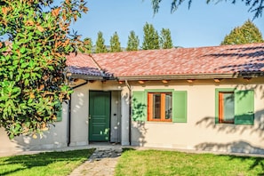 Una casa con techo de tejas, puerta verde y contraventanas en las ventanas.