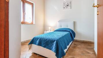 Ein Schlafzimmer mit einem Bett, einem Nachttisch, einer Lampe, einem Fenster und einem Wandbild.