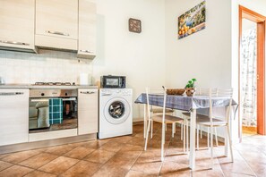 Une cuisine compacte équipée d’un lave-linge, d’un four à micro-ondes et d’un coin repas avec une table et des chaises.